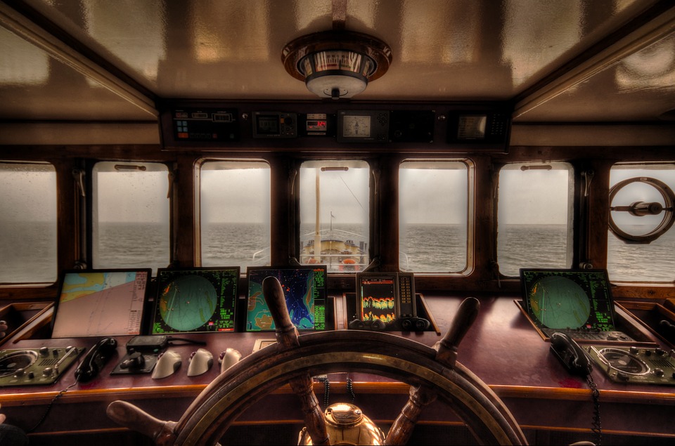 Vue sur la mer depuis la cabine d'un bateau. Au premier plan, la barre de navigation et des cartes avec des radars.