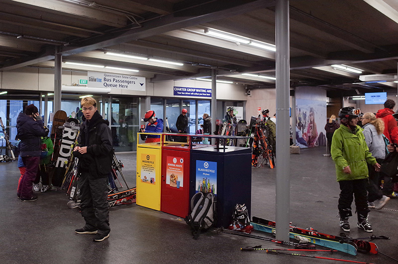 Coronet Ski Resort Entrance, Queenstown, New Zealand. Large signs indicate the queues for buses. The rubbish bins are colorful and have images and information on what to throw where.