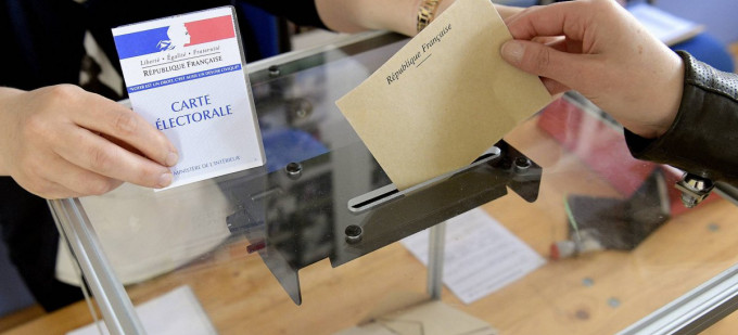 Élection en France: une main glisse une enveloppe dans un urne transparente. Une autre main tient une carte électorale